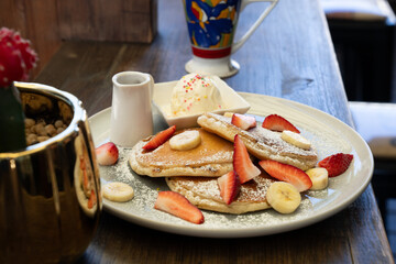 Plate of Pancakes Topped with Strawberries, Bananas, and Powdered Sugar with Ice Cream and Syrup on...