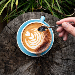 Top View of a Blue Cup with Latte Art on Rustic Wooden Table with Hand and Greenery Background  