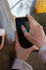 Person takes a photo with smartphone, capturing scenic outdoor view. Hands with stylish rings frame the shot. Modern technology and urban exploration. Woman photographing city.