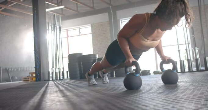 Performing push-ups using kettlebells, woman exercising in gym for fitness, copy space