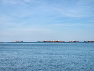 Fleet of Cargo Ships:  A fleet of cargo ships traverses the open sea, their silhouettes cutting through the blue expanse against a backdrop of a serene sky.