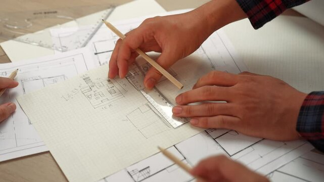 Professional engineer team discussion about house design on meeting table with architectural equipment and building blueprint scatter around at modern office. Focus on hand. Closeup. Delineation.
