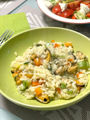 Risotto with vegetables and mussels on green plate at home. Vegetables and seafood. National cuisine of Europe. 