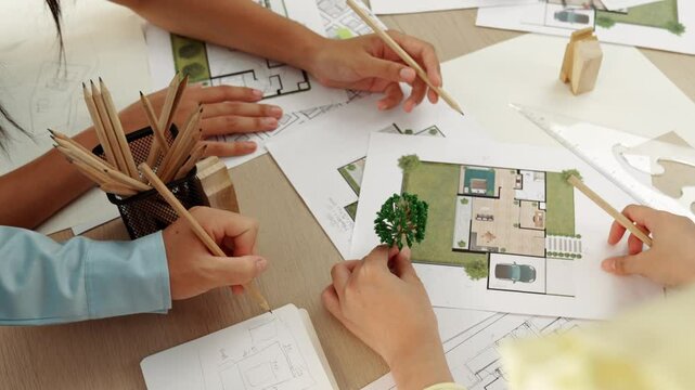 Architect and engineer use tree model discuss about building blueprint on table with architectural document, measurement tools and wooden block scatter around at modern office. Closeup. Delineation.
