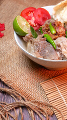Close up Beef rib soup or Iga soup clear broth with beef, potato, fresh tomato, lime, green chilies, fried onions, and crackers. Served in a white bowl with unique decoration. Space for text available