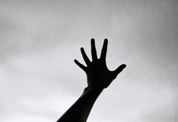 Silhouette of an outstretched hand against a cloudy sky, symbolizing reaching for hope or freedom, with a dramatic black-and-white tone.