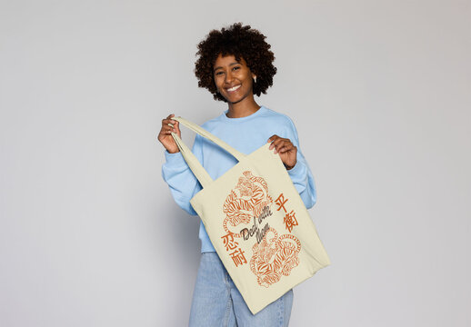 Smiling afro black woman holds a blank tote bag. PSD mockup
