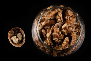 Peeled walnut fruits in a glass jar on a black background