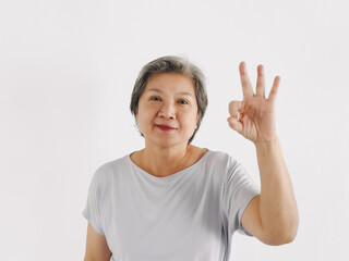 Asian elder woman showing ok sign, good job and well done hand gesture, approval or encouragement, standing isolated over white background wall.