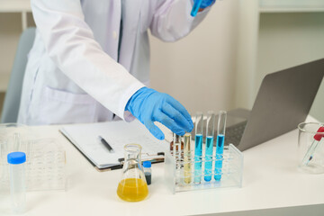Fototapeta premium Cute Caucasian schoolgirl wearing white scientist outfit carefully placing test tube into rack in science classroom. , wearing blue protective gloves, laboratory beakers, flasks, microscope.