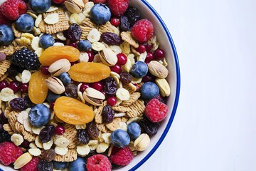 A deep dish filled with a mix of cereals, fresh berries, pistachios, dried apricots, and raisins