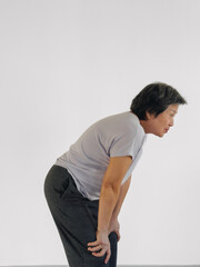 Vertical of Unhappy Asian elder woman got knee pain symptom, moaning, hand resting on both knees, standing isolated over white background wall.