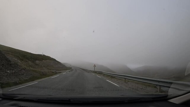 Driving through the tundra in northern Norway on E69 road. Misty surroundings with hills covered in rocks and grass, creating a tranquil and remote atmosphere.