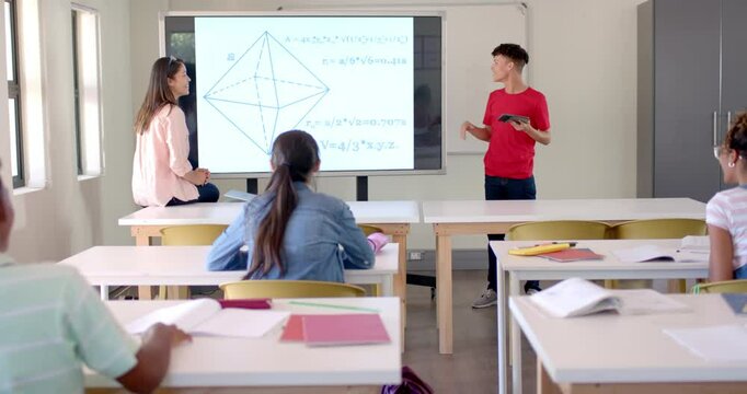 Teenage biracial boy in red shirt presents a math problem on board