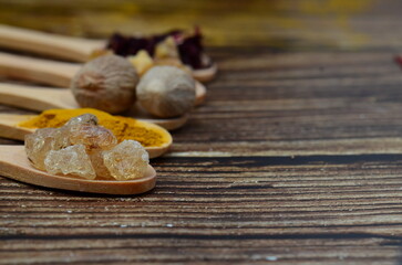 A kitchen studio food shot of various spices (Turmeric, Nutmeg, Hibiscus, Frankincense and Acacia) in a wooden spoons isolated on a wooden background.	