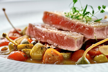 A vibrant and refreshing plate of seared tuna steak, served with cherry tomatoes, olives, and a drizzle of lemon-herb sauce