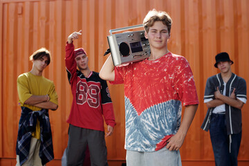 Young Men Holding Boombox Against Orange Wall Smiling