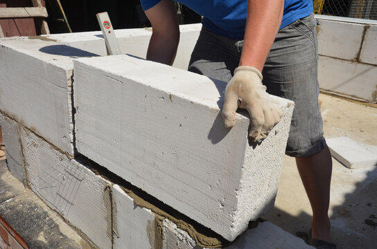 Builder contractor laying white autoclaved aerated concrete AAC blocks with concrete during house construction. Worker laying autoclaved aerated concrete blocks working with adhesive and trowel
