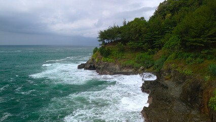 Aerial drone view of coastline with hills and trees, as well as view of coral cliffs and sea with waves from the ocean in Lampon Kebumen Central Java Indonesia