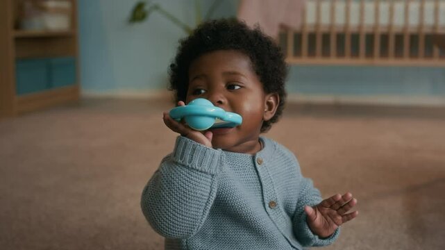 Close-up shot of cute and playful toddler chewing teething ring, while sitting on carpeted floor in her cozy nursery