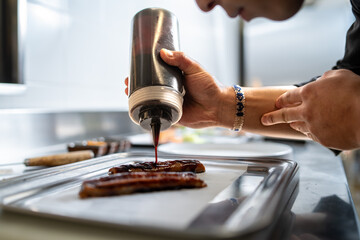 Chef drizzling soy sauce on grilled eel fillets in professional kitchen