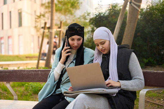 Muslim businesswomen working remotely using laptop and smartphone in a park - Powered by Adobe