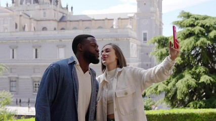 Romantic moments of a multiracial couple taking selfies and kissing near a cathedral in a city