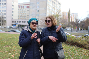 Two elderly ladies, mother and daughter, walking around the city, talking, laughing, drinking coffee. Active healthy lifestyle