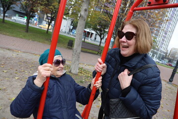 Two senior ladies enjoying ride on swings in park, elderly friends, retirement