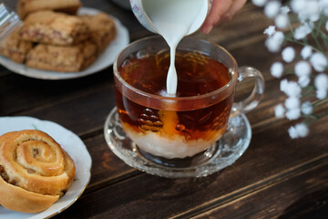 English morning breakfast. Pouring milk into mug of tea in cozy kitchen.