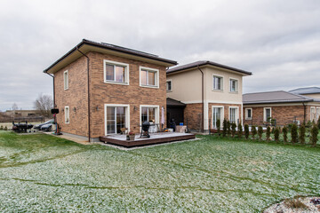 A brick house with a patio and a driveway. Modern Brick and Plaster Homes with Spacious Green Backyard Under Overcast Sky. Home Exterior