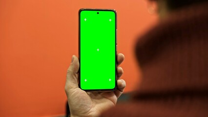 Hand of young man holding smartphone green screen in business office work. Mobile phone vertical mockup. Male person using phone with blank green background display. Chroma key smart phone. Close up.