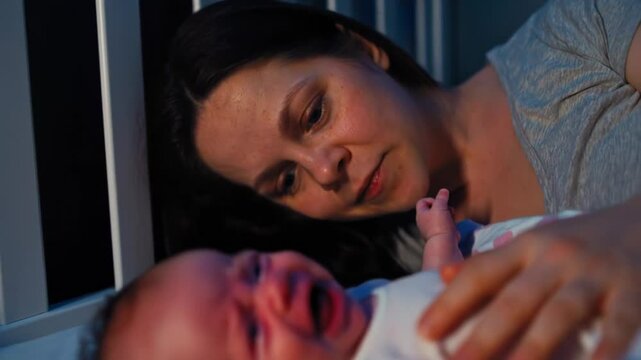 Caring mother soothing crying newborn baby in crib