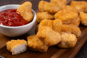  fried chicken nuggets with crumbs on a wooden board with ketchup