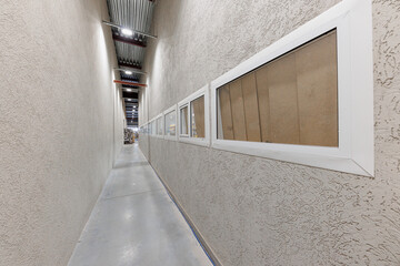 Dimly Lit Industrial Hallway A Journey Through Textured Walls and Rectangular Windows Bathed in...