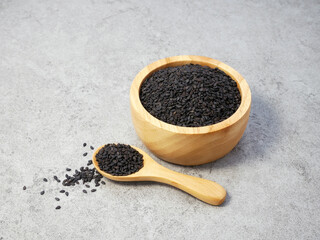 Black sesame seeds in wooden spoon and bowl on stone texture background