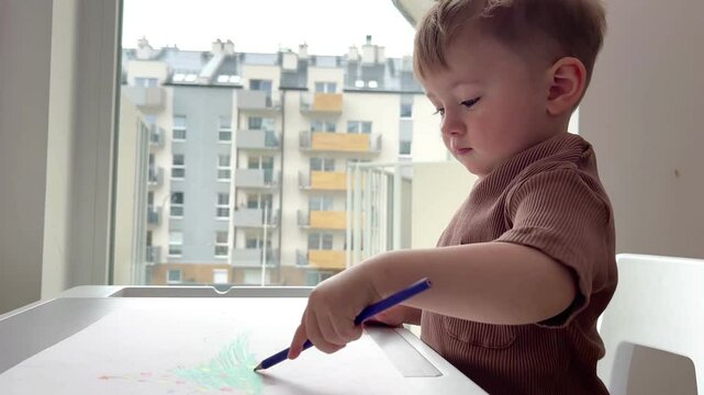 A one-and-a-half-year-old child is enthusiastically playing at the children's table, the child is learning to write and draw.