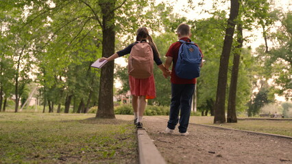 Obraz premium girl and boy with backpacks go hand hand school. teamwork. children friendship. group children go with school bags school. happy childhood. first graders park. children run class. chidhood dream