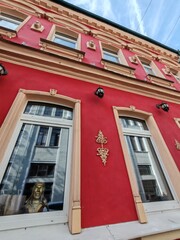 Low-angle view of a vivid red building facade with ornate beige window frames and decorative elements. The rich colors and intricate details convey urban elegance and architectural charm.