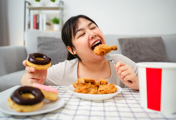 A woman is happily eating fried chicken and donuts on a plate. Fast food, Unhealthy food concept.