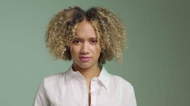 Close up of a young latin woman with curly hair expressing discontent in neutral background in studio