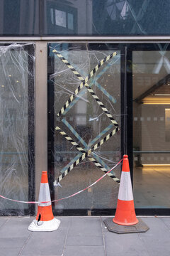 A captured moment of a glass entrance sealed with caution tape, cones, and a haunting atmosphere, evoking feelings of unease and the fragility of urban spaces.