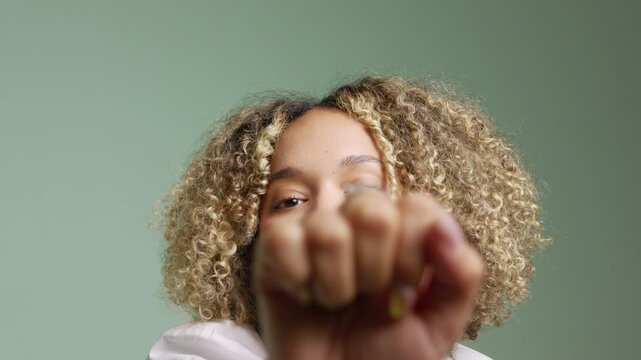 Close up of smiling young latin woman with curly hair knocking to the lens of camera in a light pastel background in studio