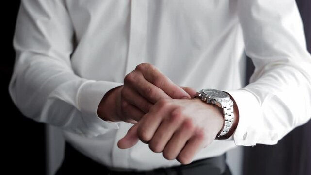 Man Adjusting Watch and Getting Dressed Elegantly, A man in a white dress shirt fastens his wristwatch while preparing for a formal event