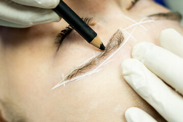 An unrecognizable beautician performs a microblading treatment on a girl's eyebrows in a beauty...
