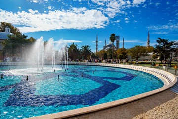 view of the fountain and Sultan Ahmet Park, Istanbul, Turkey, people walking, in the distance a mosque and urban architecture