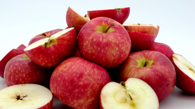 Close up of pile of whole and sliced in half red apple spinning on turn table against white background, This fruit were stored for long time and starts to going bad from inside.