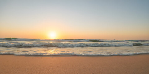 Fototapeta premium Blurred waves rolling over a vibrant sandy beach under a golden sunset, in 8K resolution