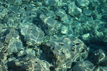 Crystal clear sea with stones on the bottom, refracting sunlight