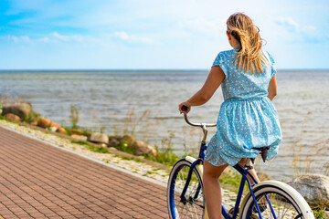 Active summer holidays. Mature woman wearing dress riding blue cruiser bike on bicycle path on...